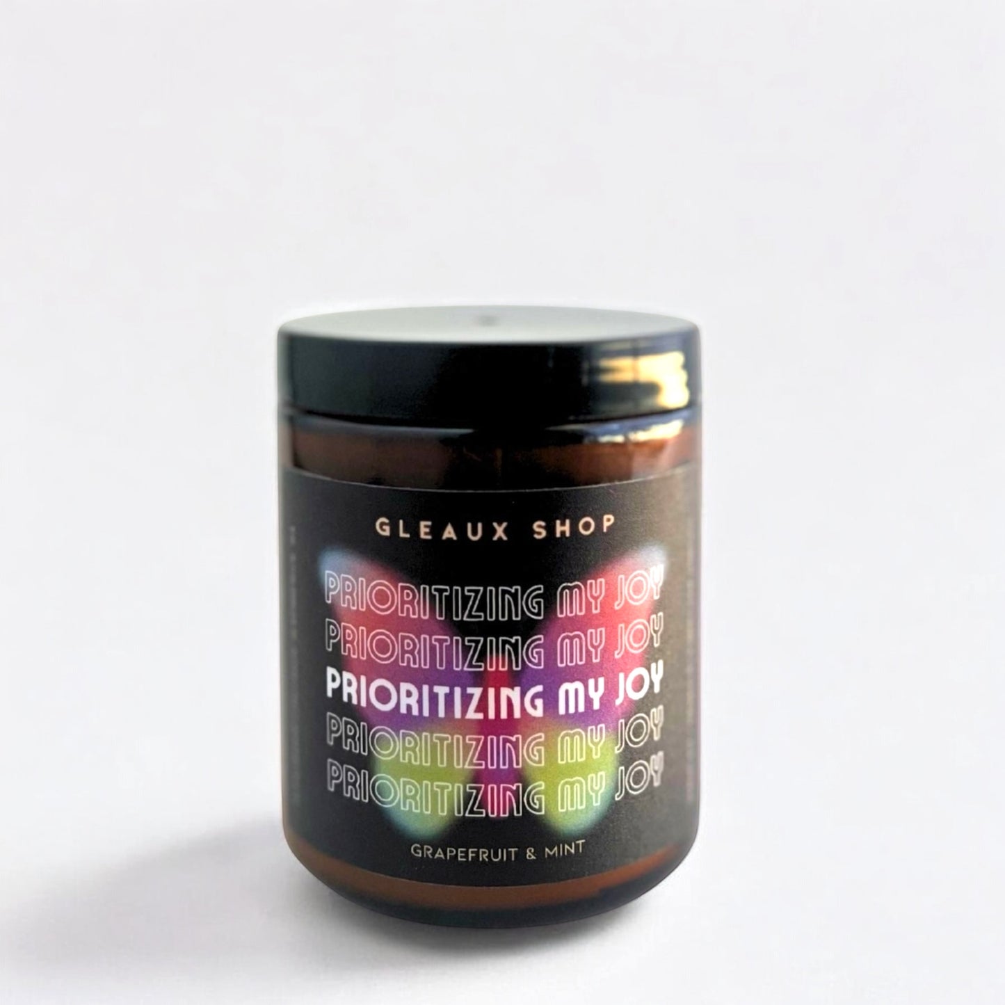 A scented coconut wax candle in an amber jar with black lid, labeled 'Gleaux Shop - Prioritizing my joy - Grapefruit & Mint'.