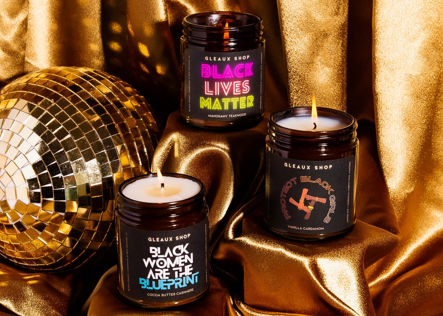 Three Gleaux Shop candles arranged on platforms with disco ball and gold fabric in the background
